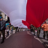 Harcerze niosą flagę przed budynkiem Ratusza
