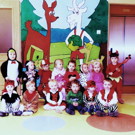 Dzieci w strojach karnawałowych siedzące na tle rysunku Koziołka Matołka