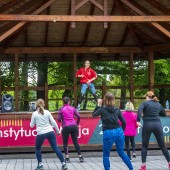 zajęcia w parku - na scenie instruktorka zumby, obok sceny ćwiczące osoby